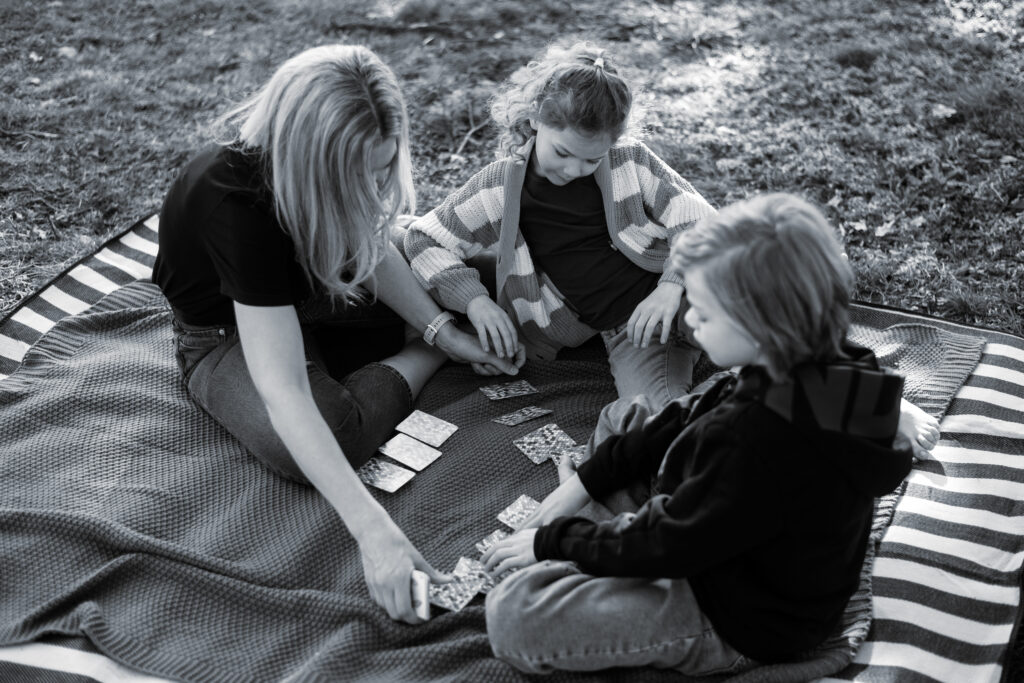 Zwei Kinder sitzen mit ihrer Mutter auf einer Picknickdecke beim Spielen in der Natur bei Ingolstadt